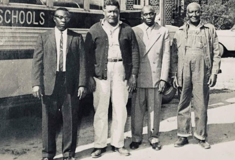 4 bus drivers in front of a school bus.