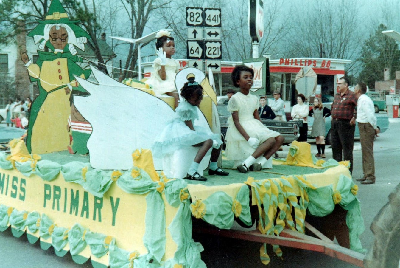 3 young girls sit on a homecoming float that says Miss Primary